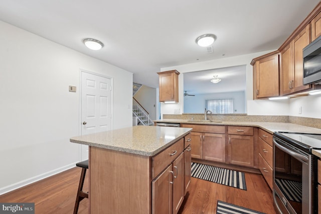 kitchen featuring appliances with stainless steel finishes, a breakfast bar, sink, a center island, and dark wood-type flooring