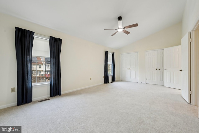 unfurnished bedroom with light carpet, ceiling fan, lofted ceiling, and multiple closets