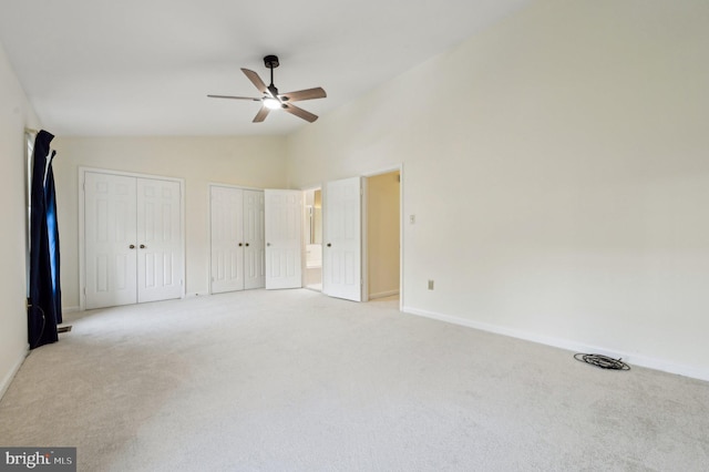 unfurnished bedroom featuring light carpet, two closets, lofted ceiling, and ceiling fan