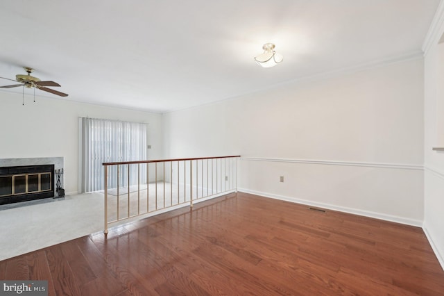 empty room featuring crown molding, a high end fireplace, wood-type flooring, and ceiling fan