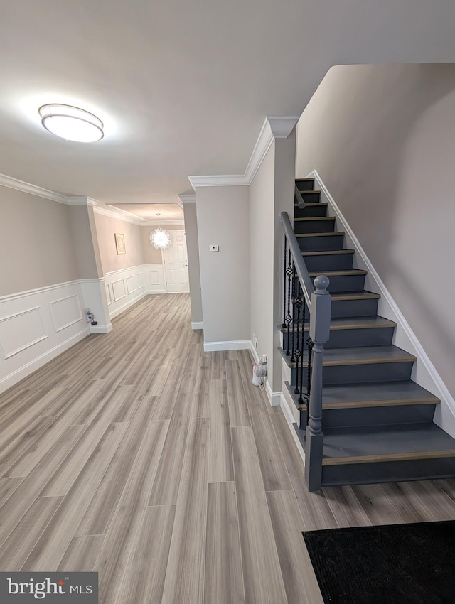 staircase with hardwood / wood-style flooring, ornamental molding, and a chandelier