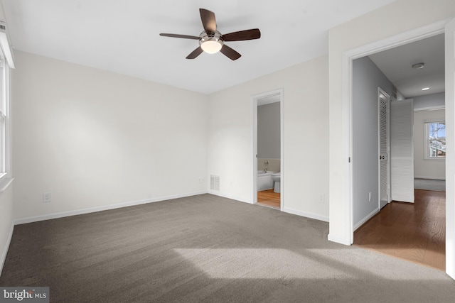 unfurnished bedroom featuring ceiling fan, ensuite bath, and dark colored carpet