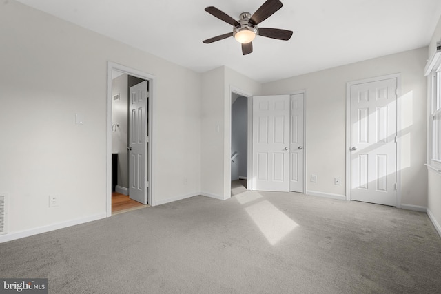 unfurnished bedroom featuring connected bathroom, light colored carpet, multiple closets, and ceiling fan