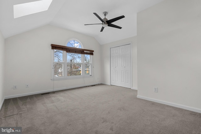 unfurnished bedroom with ceiling fan, a closet, vaulted ceiling with skylight, and carpet flooring