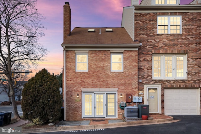 back house at dusk with a garage, central AC unit, and french doors