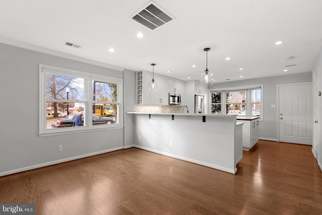 kitchen with pendant lighting, a breakfast bar area, appliances with stainless steel finishes, white cabinets, and kitchen peninsula