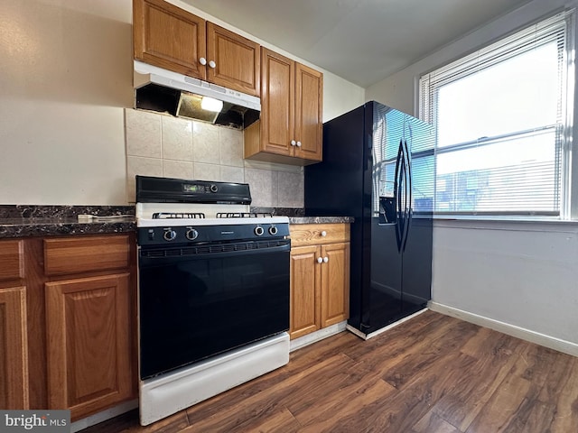 kitchen with black fridge, tasteful backsplash, dark hardwood / wood-style floors, dark stone counters, and gas range oven