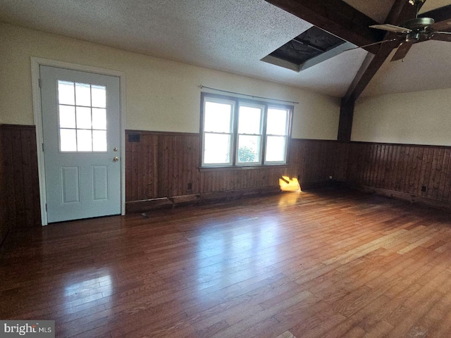 unfurnished room with wood-type flooring, vaulted ceiling with beams, ceiling fan, and a textured ceiling