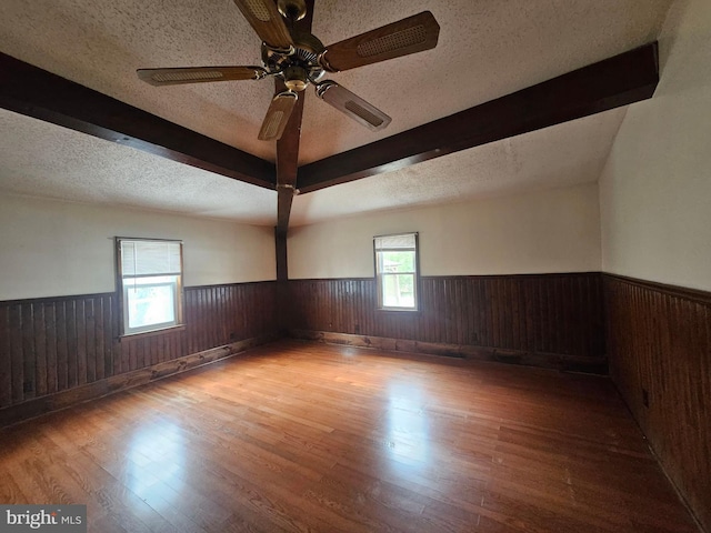 empty room with beamed ceiling, ceiling fan, a textured ceiling, and light hardwood / wood-style flooring