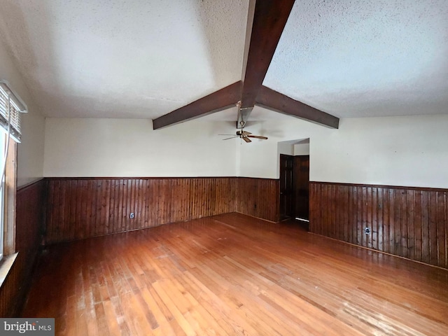 unfurnished room featuring ceiling fan, hardwood / wood-style flooring, lofted ceiling with beams, and a textured ceiling