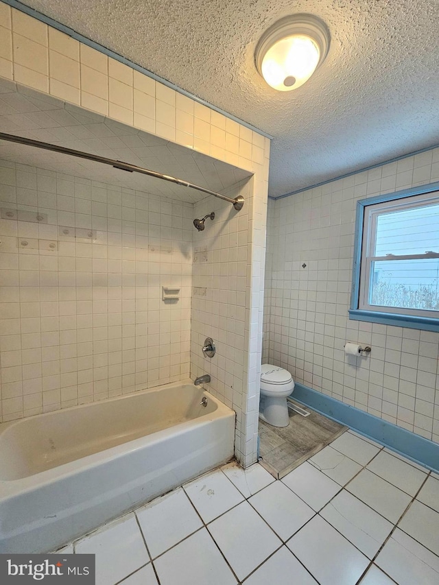 bathroom with tiled shower / bath, tile walls, tile patterned flooring, toilet, and a textured ceiling