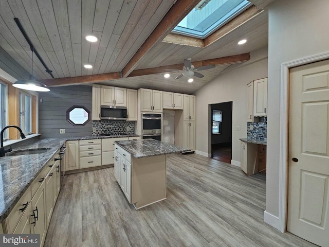 kitchen with dark stone countertops, sink, stainless steel appliances, and vaulted ceiling with skylight