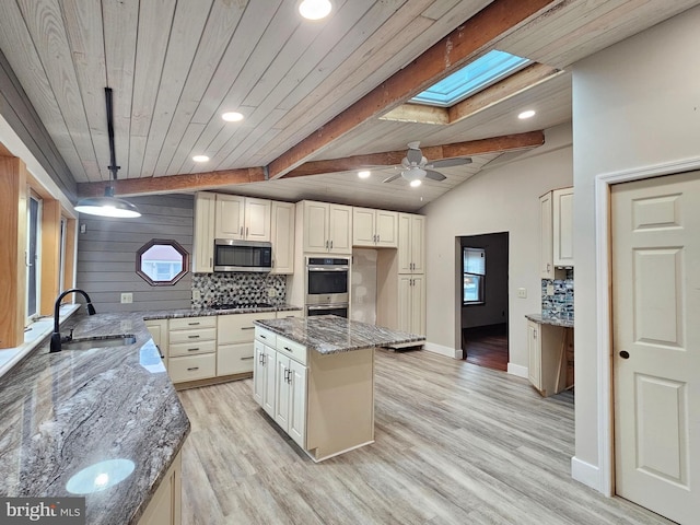 kitchen with sink, lofted ceiling with skylight, dark stone counters, and appliances with stainless steel finishes