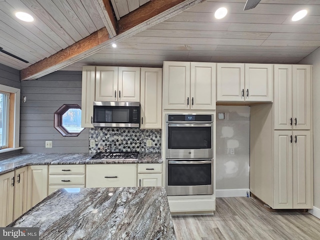 kitchen featuring beamed ceiling, appliances with stainless steel finishes, dark stone countertops, and light hardwood / wood-style floors