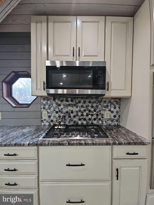 kitchen with white cabinetry, stainless steel appliances, tasteful backsplash, and dark stone counters