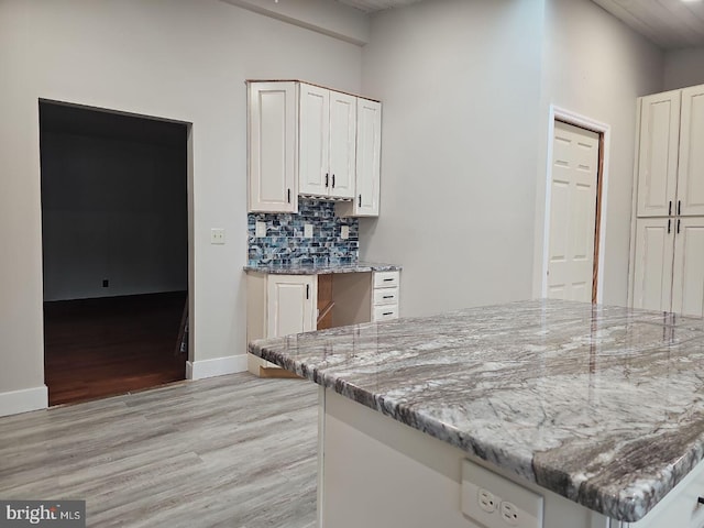 kitchen featuring light stone counters, white cabinetry, light hardwood / wood-style floors, and decorative backsplash