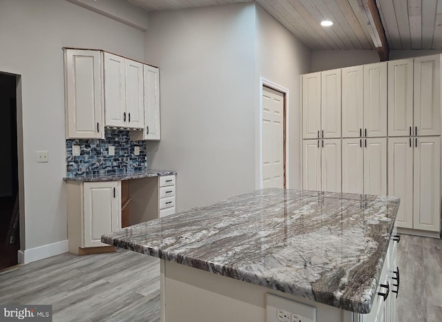 kitchen with a kitchen island, white cabinetry, decorative backsplash, light stone countertops, and light hardwood / wood-style flooring