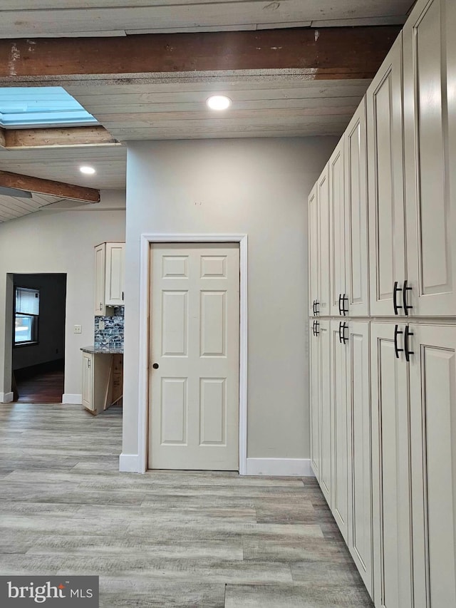 hallway featuring vaulted ceiling with skylight and light hardwood / wood-style flooring