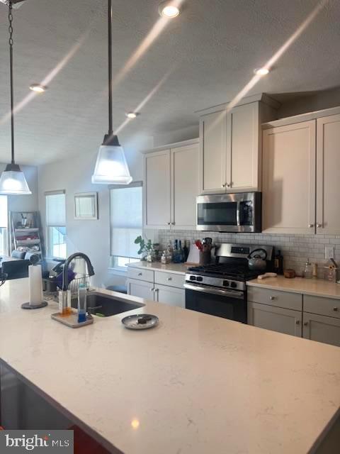 kitchen featuring appliances with stainless steel finishes, pendant lighting, sink, decorative backsplash, and a center island with sink