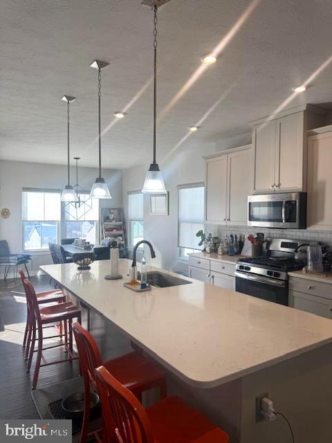 kitchen featuring sink, white cabinets, decorative backsplash, a kitchen island with sink, and stainless steel appliances