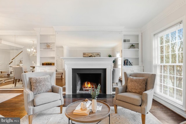 sitting room featuring hardwood / wood-style flooring, ornamental molding, built in features, and an inviting chandelier