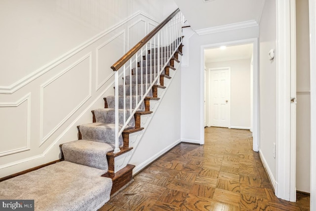 staircase with crown molding and parquet flooring