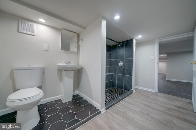 bathroom featuring a tile shower, sink, hardwood / wood-style floors, and toilet