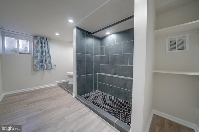 bathroom with wood-type flooring, toilet, and a tile shower