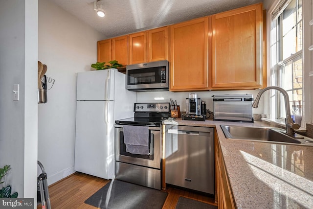 kitchen with appliances with stainless steel finishes, sink, hardwood / wood-style flooring, light stone counters, and a textured ceiling