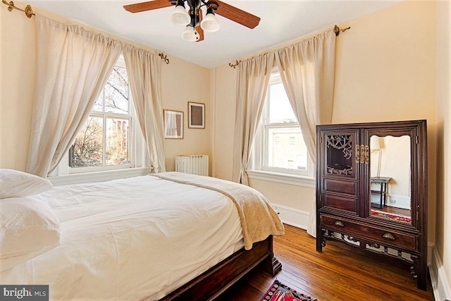 bedroom featuring hardwood / wood-style flooring, ceiling fan, radiator heating unit, and multiple windows