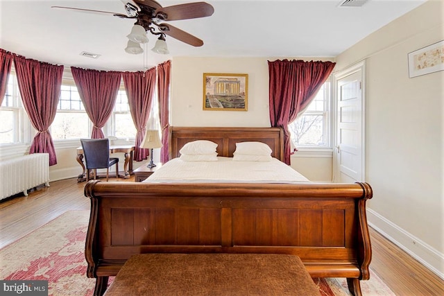 bedroom with multiple windows, ceiling fan, radiator heating unit, and wood-type flooring