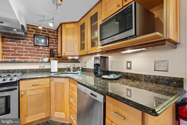 kitchen with sink, stainless steel appliances, dark stone counters, and wall chimney exhaust hood