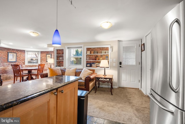 kitchen featuring brick wall, dark stone countertops, stainless steel fridge, hanging light fixtures, and light carpet