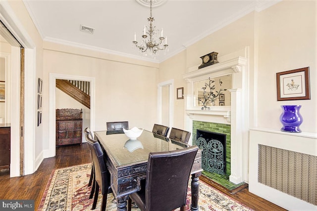 dining space with an inviting chandelier, a brick fireplace, crown molding, and dark wood-type flooring