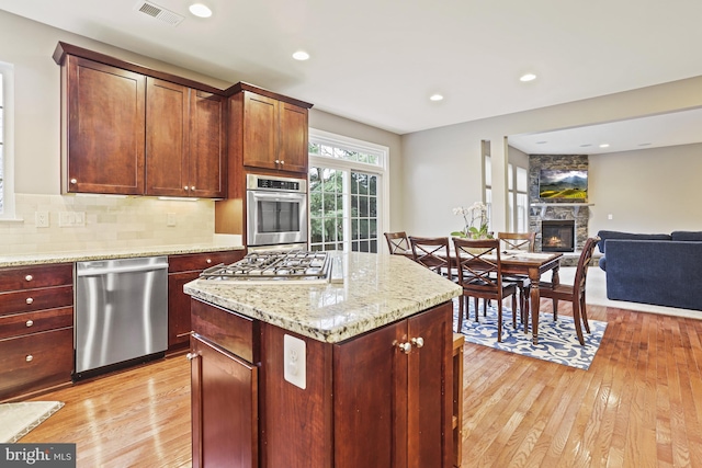 kitchen featuring a stone fireplace, decorative backsplash, stainless steel appliances, light stone countertops, and light wood-type flooring