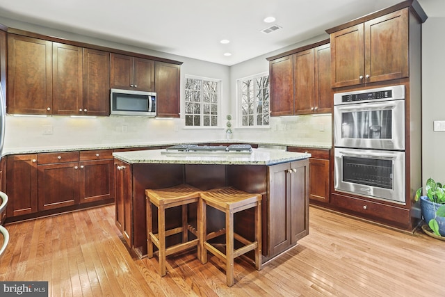 kitchen with stainless steel appliances, a kitchen island, light stone countertops, and light wood-type flooring