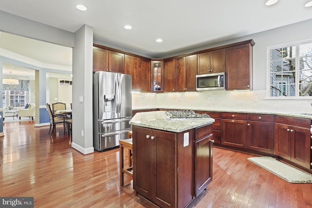 kitchen with stainless steel appliances, light stone counters, a kitchen island, decorative backsplash, and light wood-type flooring