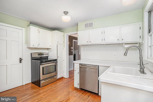 kitchen with sink, light hardwood / wood-style flooring, white cabinets, and appliances with stainless steel finishes