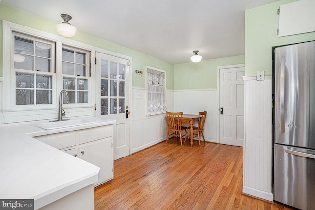 kitchen with stainless steel refrigerator, sink, light hardwood / wood-style flooring, and white cabinets