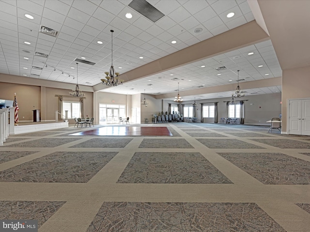 interior space featuring a towering ceiling, plenty of natural light, a drop ceiling, and a notable chandelier