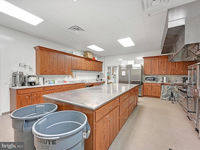 kitchen with a spacious island, sink, stainless steel appliances, a drop ceiling, and wall chimney exhaust hood