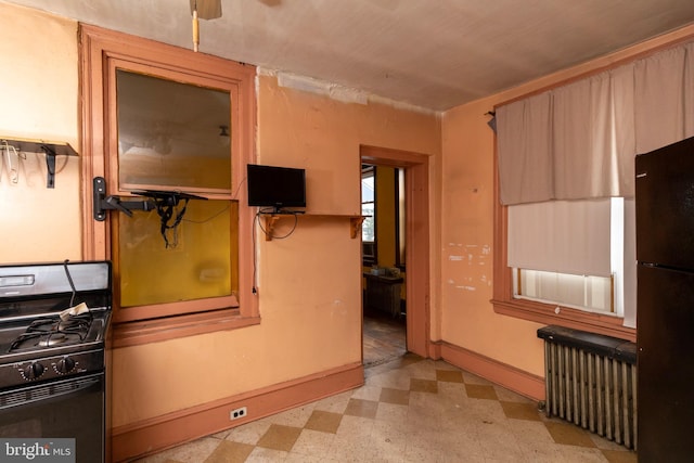 kitchen with radiator heating unit, light brown cabinets, and black appliances