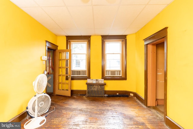 empty room featuring radiator, dark wood-type flooring, and a drop ceiling