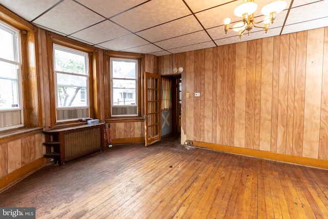 spare room featuring radiator heating unit, wooden walls, a chandelier, and hardwood / wood-style floors