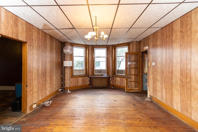 unfurnished room with an inviting chandelier, dark hardwood / wood-style floors, radiator heating unit, and wooden walls