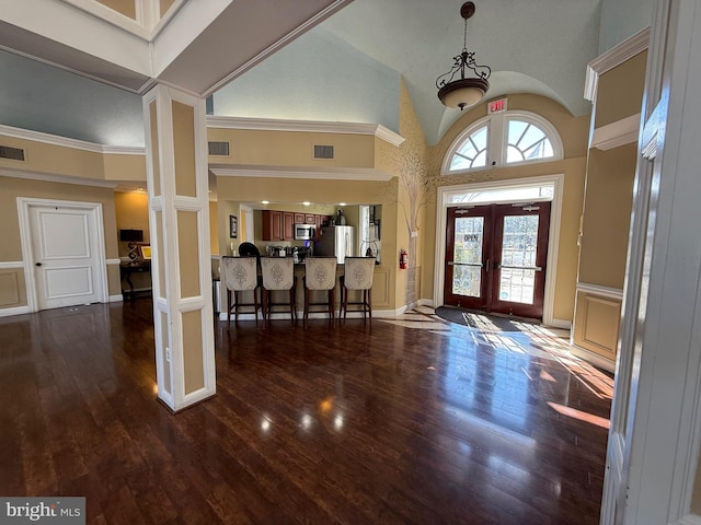 entrance foyer featuring ornate columns, dark hardwood / wood-style floors, high vaulted ceiling, and french doors