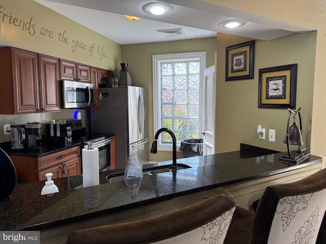 kitchen featuring sink, a breakfast bar, appliances with stainless steel finishes, kitchen peninsula, and dark stone counters