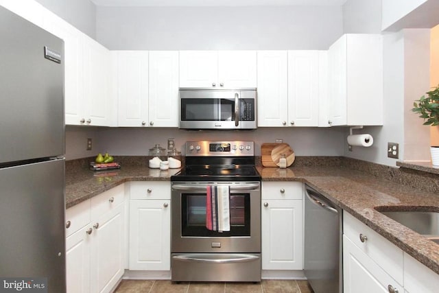 kitchen with dark stone countertops, light tile patterned flooring, white cabinets, and appliances with stainless steel finishes