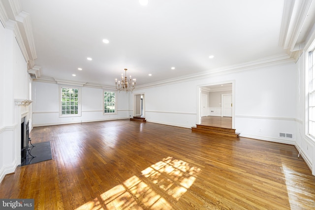 unfurnished living room featuring a notable chandelier, visible vents, a fireplace with flush hearth, ornamental molding, and wood finished floors