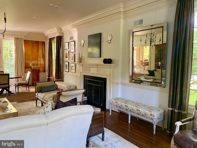 living area with crown molding, a notable chandelier, a fireplace, visible vents, and wood finished floors